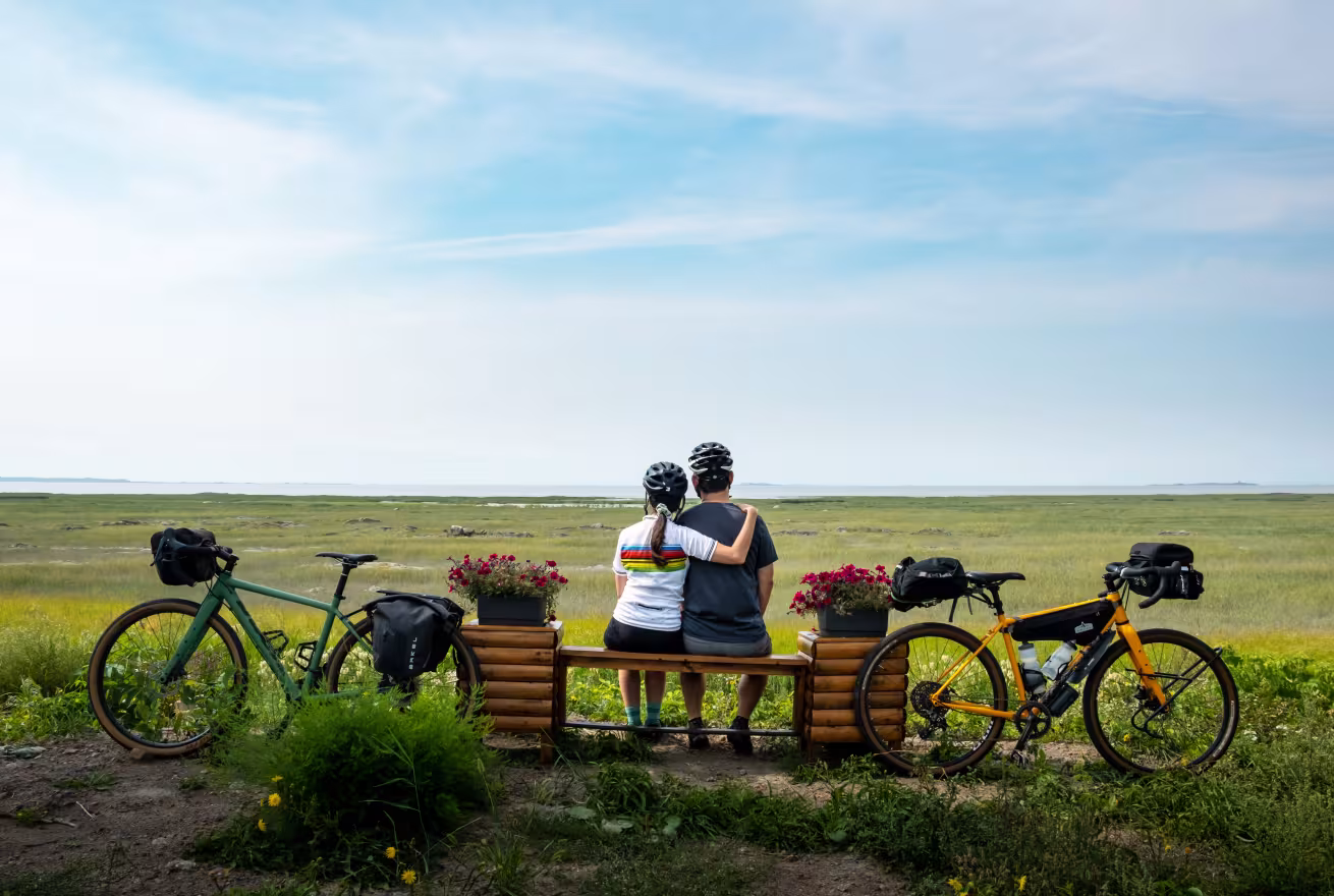 Deux cyclistes sont assis sur un banc à L'Islet-sur-Mer face au fleuve Saint-Laurent, région de Chaudière-Appalaches
