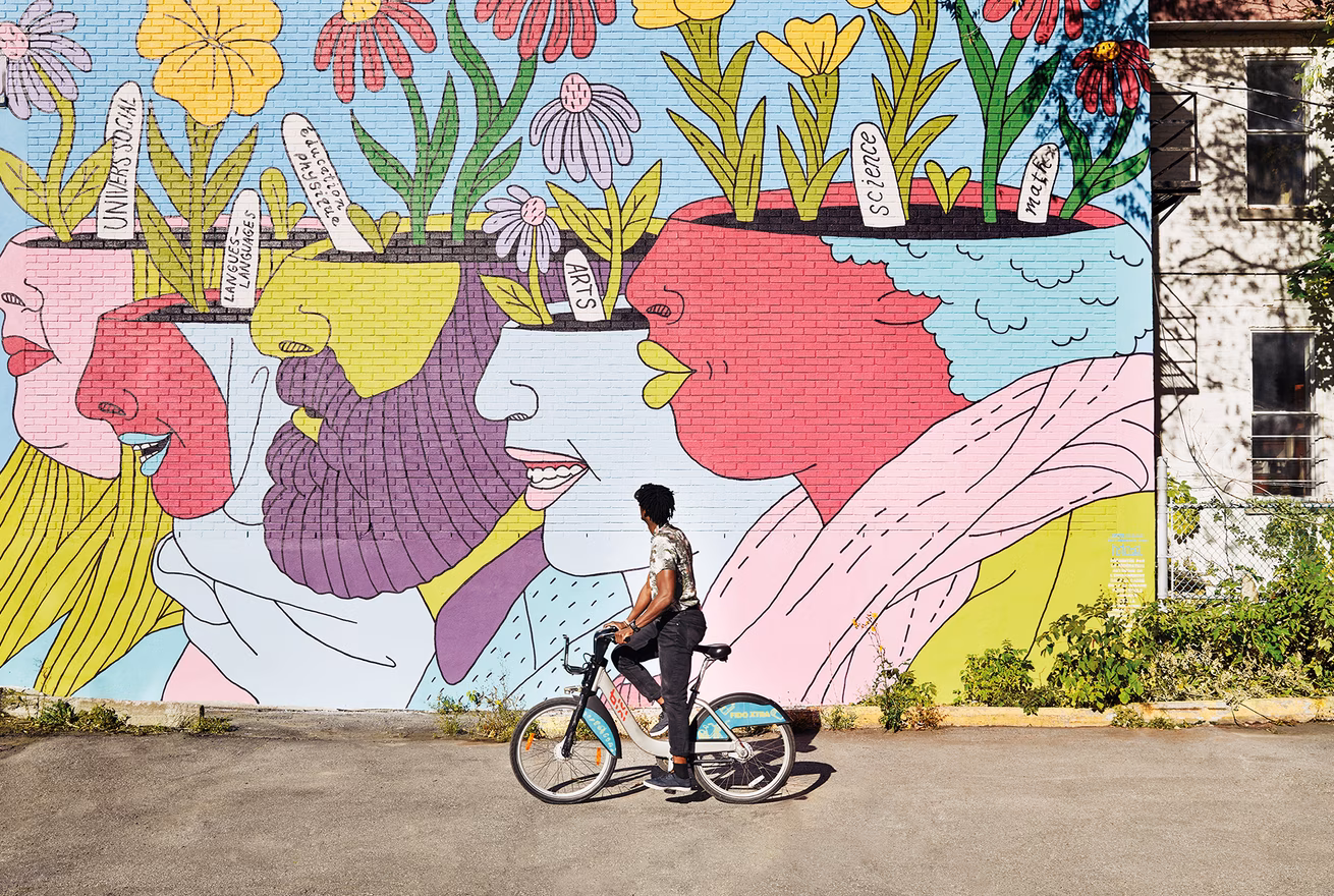 Un cycliste avec Bixi se tient devant une murale de Montréal