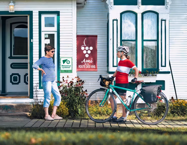Une aubergiste attestée Bienvenue cyclistes! accueille une cycliste en cyclotourisme pour passer la nuit dans son établissement.