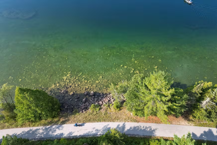 Un cycliste longe un lac turquoise sur la Véloroute des Draveurs